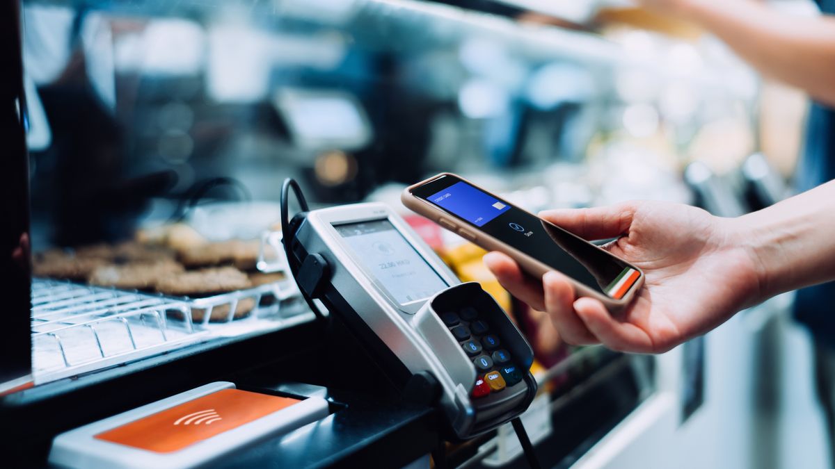 Close up of a woman's hand paying with her smartphone in a cafe, scan and pay a bill on a card machine making a quick and easy contactless payment. NFC technology, tap and go conceptClose up of a woman's hand paying with her smartphone in a cafe, scan and pay a bill on a card machine making a quick and easy contactless payment. NFC technology, tap and go conceptd3sign