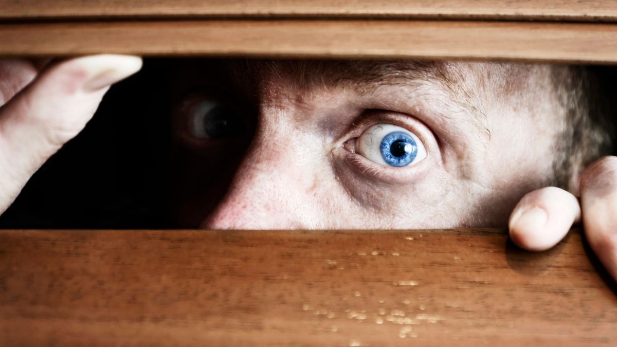 Wystraszony mężczyzna patrzy przez drewniane żaluzje w oknie