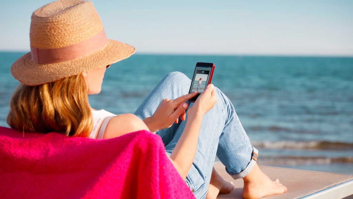 Rear view portrait of relaxed woman watching photos on her mobile phone while relaxing on sunbed on the beach.portrait, woman, summer, beach, beautiful, travel, mobile phone, telephone, handy, smartphone, holding, hand, using, wifi, touching, screen, happiness, happy, sunglasses, straw hat, mobile phone, telephone, handy, smartphone, using, holding, hand, blue sky, sunny, casual, confident, sunbad, mobile app, towel, vacation, watching, holiday, healthy, sandy, lifestyle, looking, mature, middle aged, 40s, 50s, enjoying, outdoor, people, person, relaxing, smiling, sunlight, wellbeing, seaside, traveling, resort, day, sunbathing, weekend, day, nature, water, sun, female, barefoot