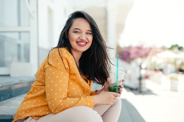 moda Plus size woman walking down city and drinking healthy spinach smoothie in plastic cup with strawAlena Ozerovaplus, size, woman, fashion, model, style, street, summer, cocktail, smoothie, everyday, girl, overweight, plump, healthy, vegan, diet, city, drink, urban, cool, fun, modern, lady, happy, outside, shake, straw, fruit, walking, daily, juice, herbal, person, cold, energy, holding, life, beverage, lifestyle, takeaway, fresh, yellow, background, wall, smile, away, take, tourist, spinach