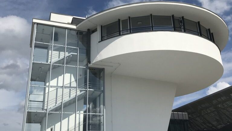 Nowoczesny budynek z przeszkloną fasadą i spiralnymi schodami, otoczony ogrodzeniem budowlanym.