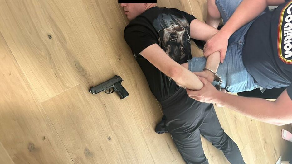 Mężczyzna leżący na podłodze z rękami związanymi kajdankami, obok niego leży pistolet.