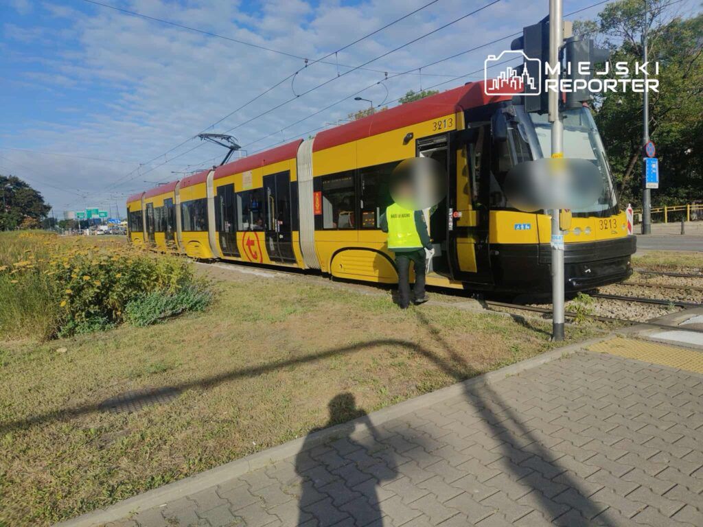 Tramwaj w żółto-czerwonym malowaniu stoi na przystanku, a pracownik w kamizelce podchodzi do drzwi.