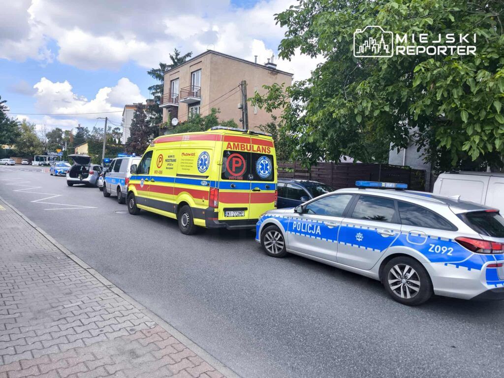 Karetkę pogotowia oraz radiowozy policji zaparkowane na ulicy w pobliżu budynków mieszkalnych.
