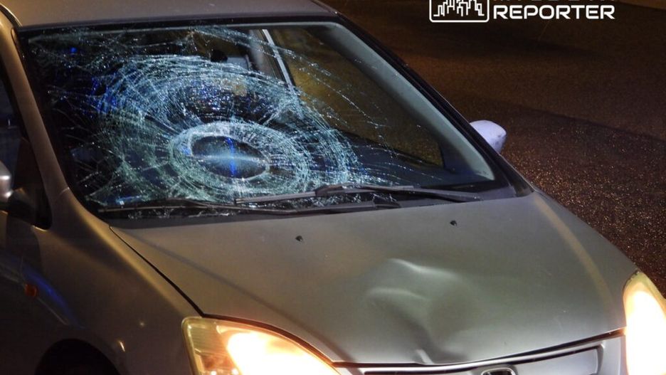 Uszkodzony samochód z wgniecioną maską i pękniętą szybą przednią w nocy na oświetlonej ulicy.