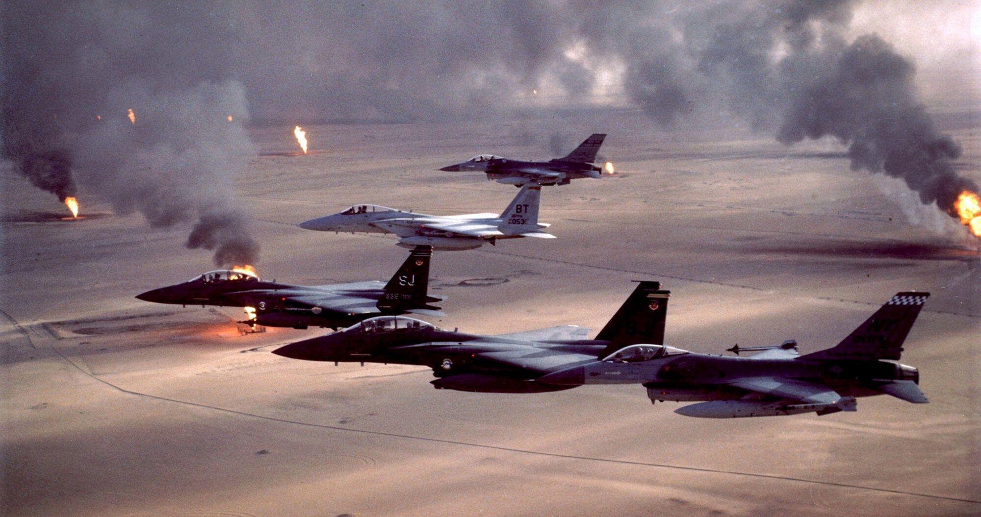 1991 rok, operacja "Pustynna Burza", czyli pierwsza wojna w Iraku, militarnie wygrana przez USA, które jednak pozostawiły Saddama Husajna przy władzy. Na zdjęciu myśliwce F-16A Fighting Falcon, F-15E Strike Eagle i F-15C Eagle, lecące nad płonącymi polami naftowymi Kuwejtu