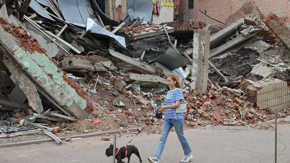Kobieta spaceruje z psem obok budynku zniszczonego przez rosyjski ostrzał, Okhtyrka, region Sumy, północno-wschodnia Ukraina.