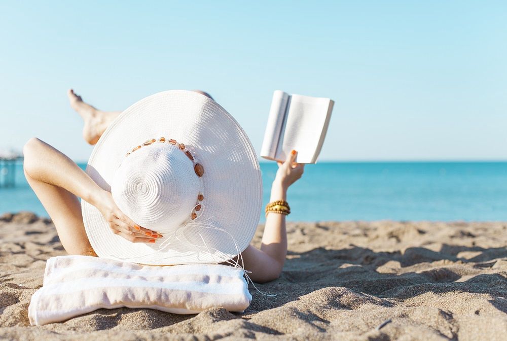 A woman is sunbathing on the beach in a hat and reading a book (illustrative photo)