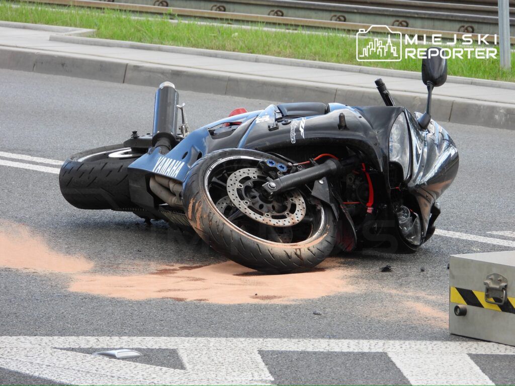 Motocykl leżący na boku na drodze, obok widoczny proszek absorbujący płyny.