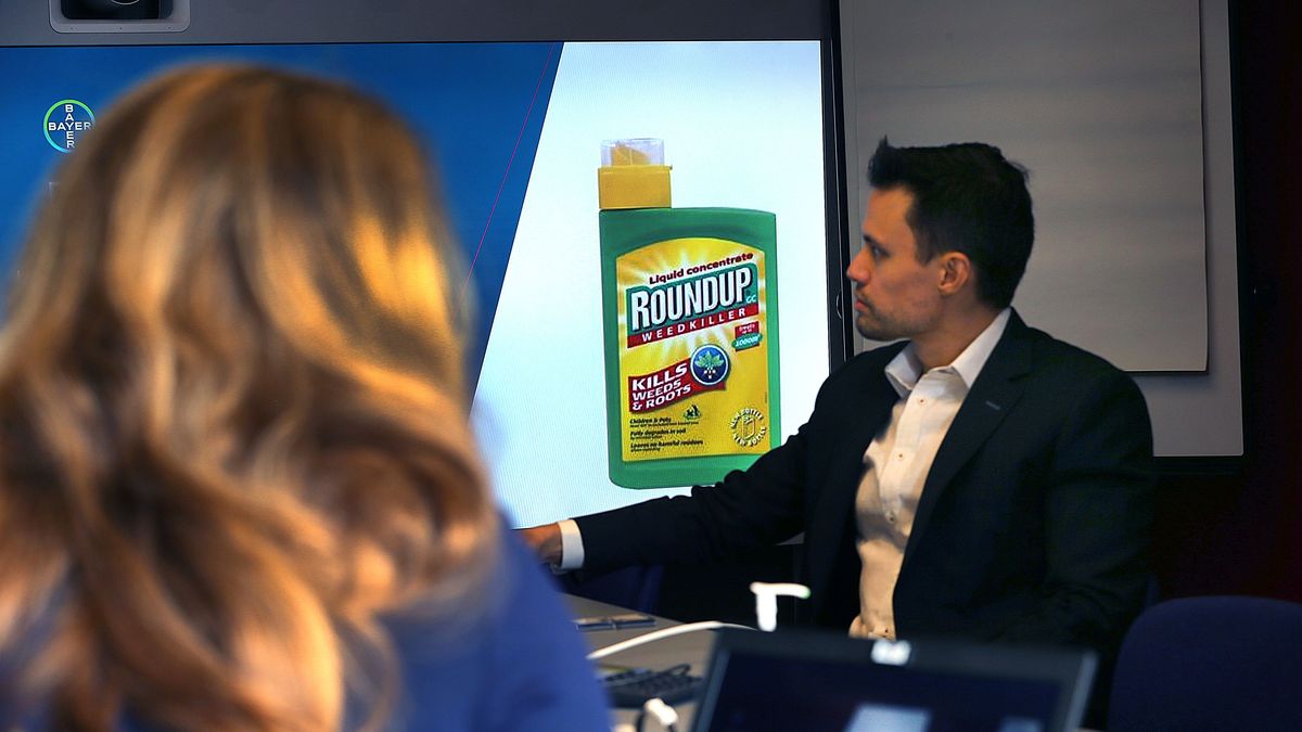 CAMBRIDGE, MA - DECEMBER 10: Dan Childs, Director of US External Communications for Bayer, sits in front of a screen as Bayer's Dr. S. Eliza Dunn, left, shows a bottle of Roundup during her presentation at Bayer's Cambridge, MA facility on Dec. 10, 2019. Dunn, a physician who works for Bayer, said Tuesday that theres no credible evidence the German companys signature weedkiller endangers consumers, and that banning Roundup would be disastrous for farmers and the planet. Three juries recently delivered staggering multimillion-dollar verdicts to people who claimed Roundup weedkiller caused their cancer. A 2015 finding by a World Health Organization agency that Roundups active ingredient, glyphosate, is probably carcinogenic to humans. (Photo by John Tlumacki/The Boston Globe via Getty Images)