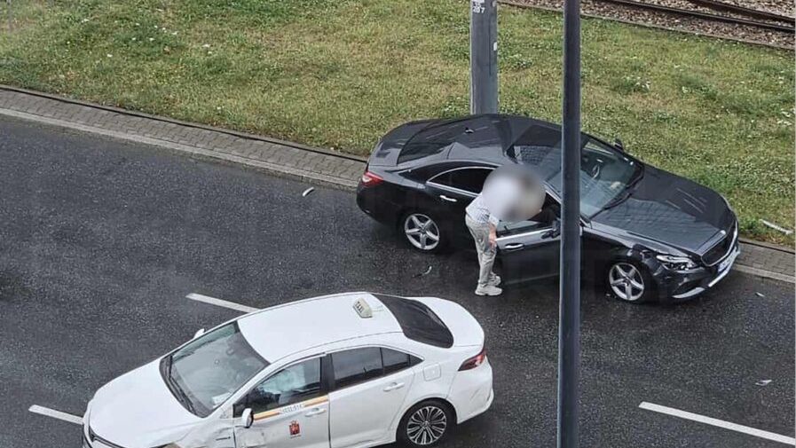 Czarny samochód osobowy stoi na jezdni, a obok niego mężczyzna sprawdzający uszkodzenia białego taxi po kolizji.