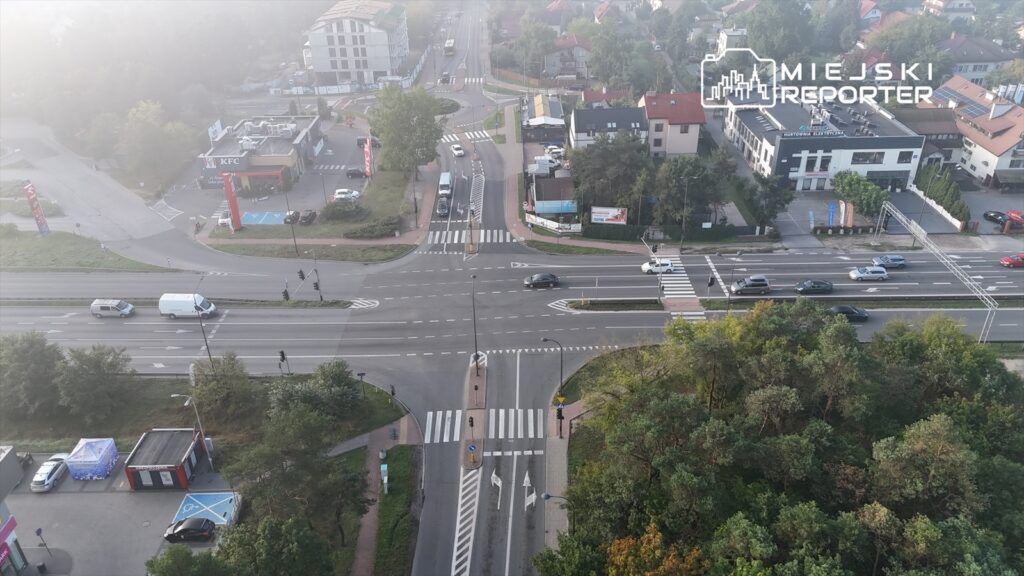 Rondo z ruchem samochodowym, w tle restauracja KFC oraz nowoczesne budynki mieszkalne. Widok z lotu ptaka.