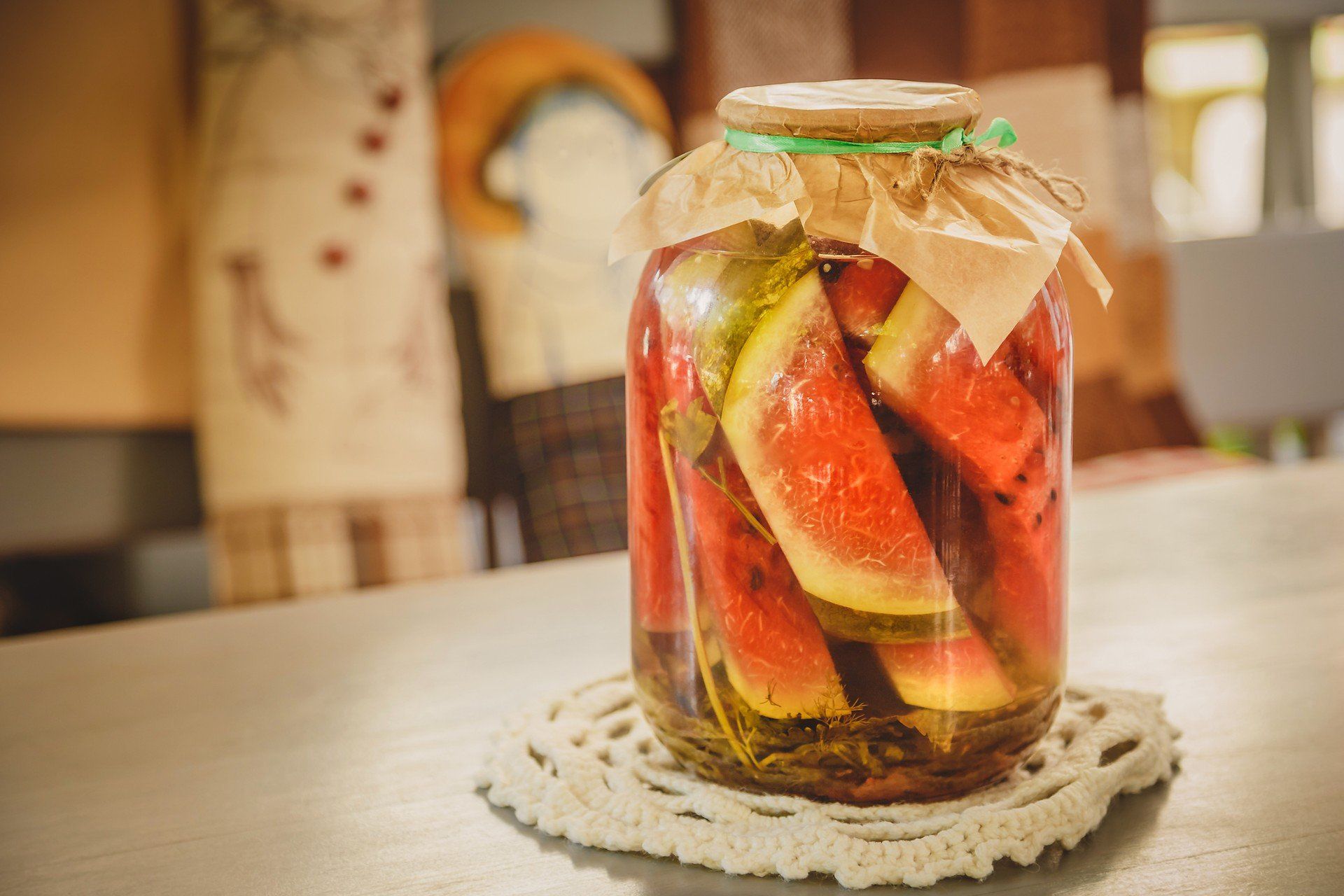 Marinated or pickled watermelon with herbs in a glass jar on a wooden table in a kitchen.
