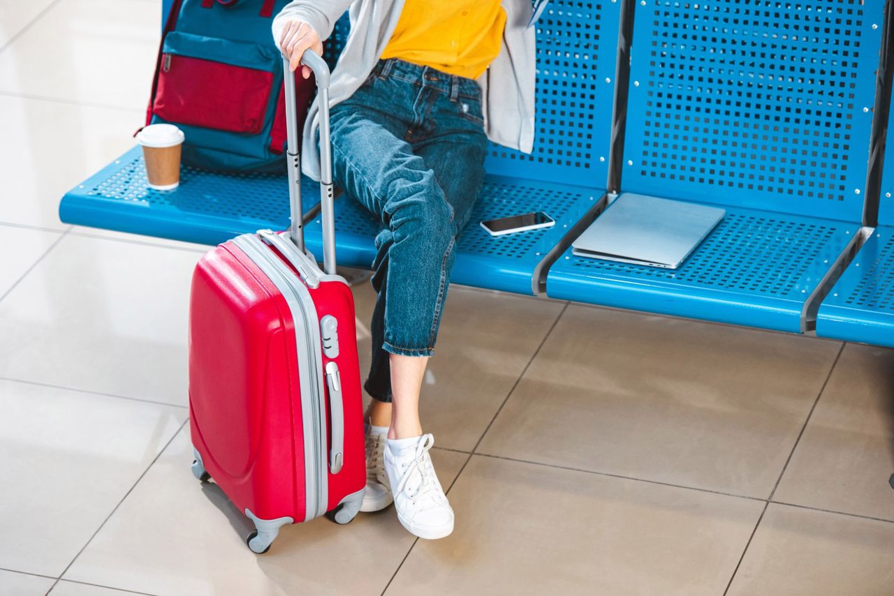 <p>cropped view of woman with luggage near backpack laptop and smartphone</p>
