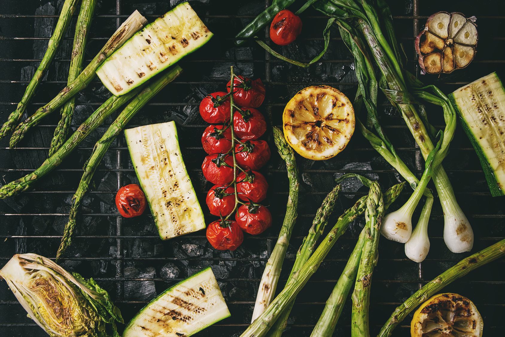 Grilled vegetables green asparagus, garlic, lemon, spring onion, zucchini, cherry tomatoes, salad on bbq grill rack over charcoal. Top view. Barbecue concept