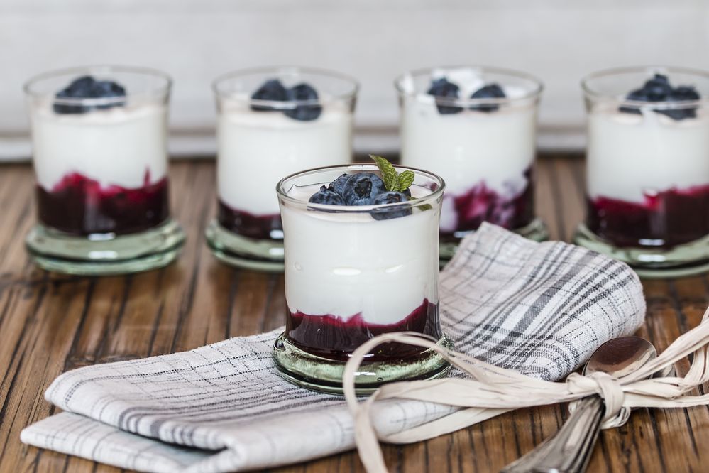 Yogurt with fresh blueberries and blueberries jam, in glass bowl over old wood background, with some glasses more at bottom. 
