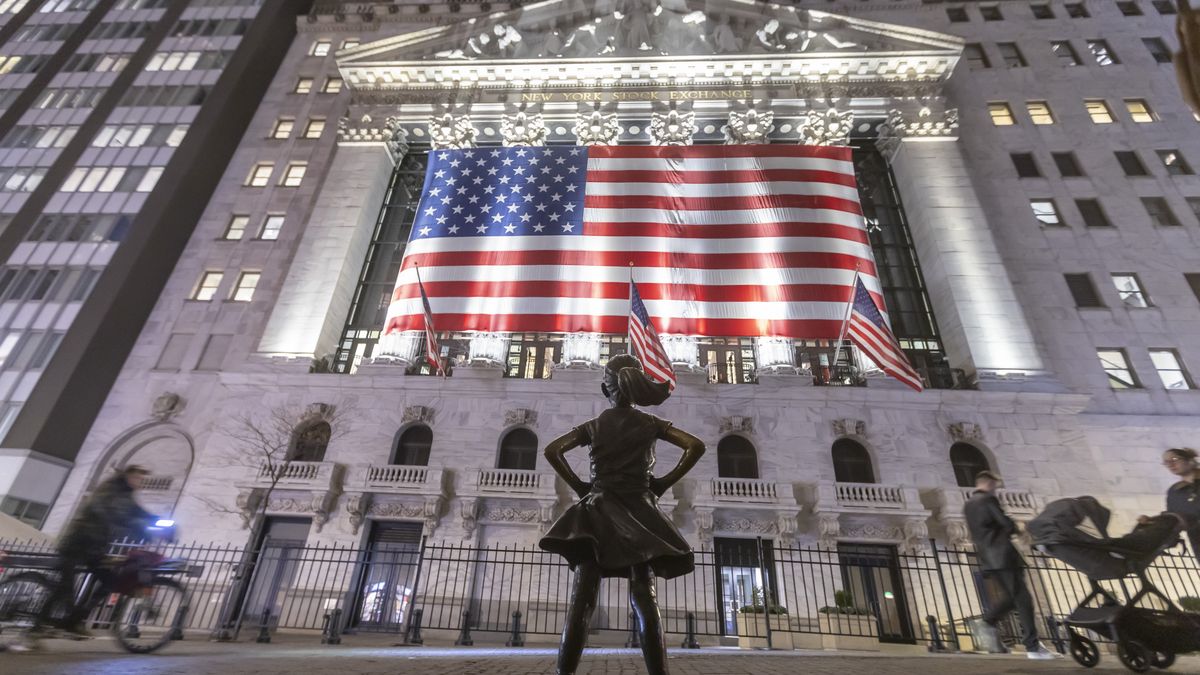 The Fearless Girl bronze sculpture by Kristen Visbal, stands across the New York Stock Exchange building and people are passing by. Night view of the illuminated exterior of New York Stock Exchange with a big American flag from the front facade. NYSE building has the style of classical architecture of Greece with columns, the inscription New York Stock Exchange and US flags hanging. The financial organization at Wall Street is a symbol for the global and American Economy as one of the most powerful financial institution located in Wall Street at lower Manhattan in New York City, United States of America. The US stock market is reacting with heavy losses after president Trump tariffs announcement on April 2025. November 2024 in NYC, USA  (Photo by Nicolas Economou/NurPhoto via Getty Images)