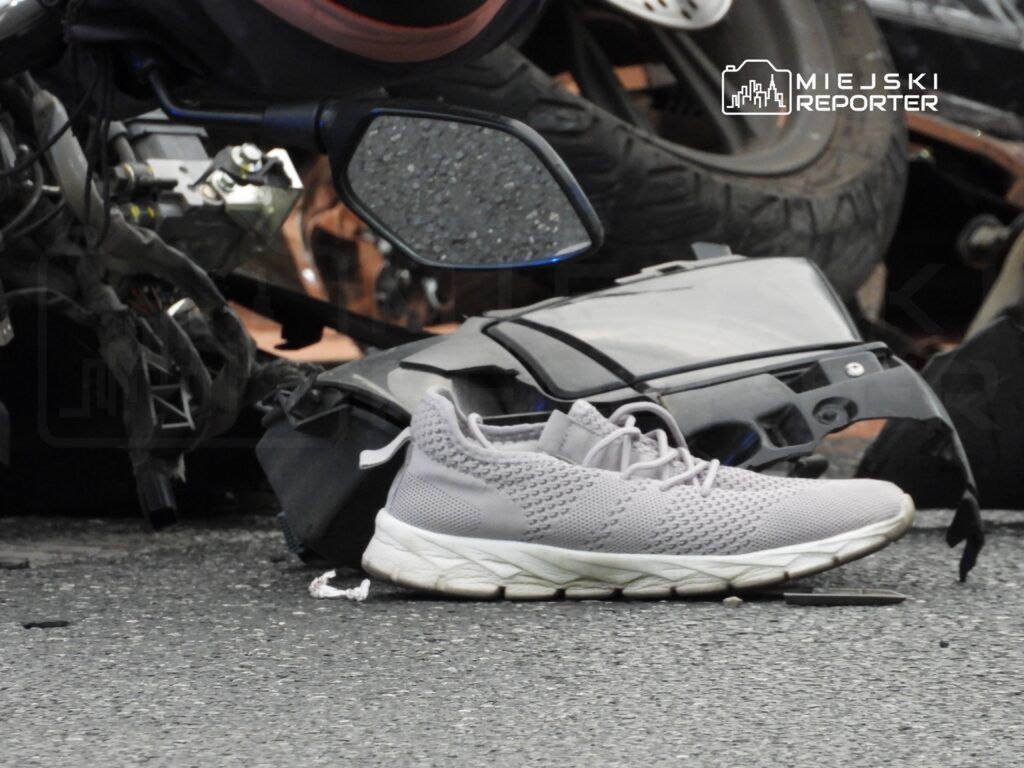 Szary but sportowy leży na drodze obok uszkodzonego motocykla i fragmentów pojazdu.