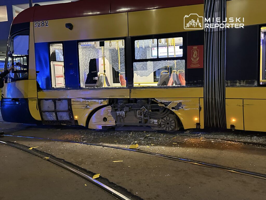 Zniszczony tramwaj z wybitymi szybami stoi na torach, obok leżą fragmenty szkła oraz żółte elementy.