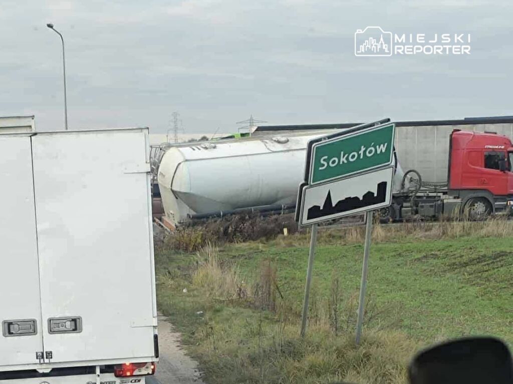 Cysterna przewrócona na poboczu drogi obok znaku miejscowości Sokołów, w tle ciężarówki na drodze.