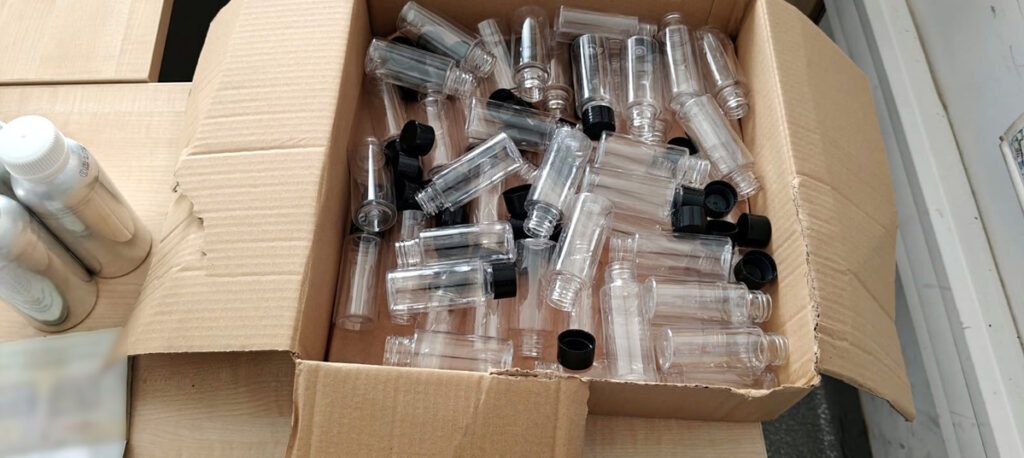 Pudełko z przezroczystymi butelkami plastikowymi i czarnymi zakrętkami, leżące na drewnianej powierzchni.