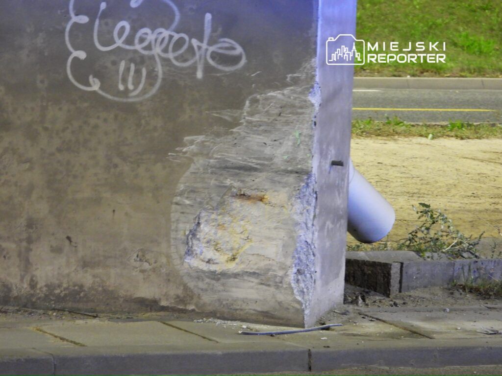 Zniszczony narożnik betonowego słupa z widocznymi uszkodzeniami i graffiti w miejskim otoczeniu.