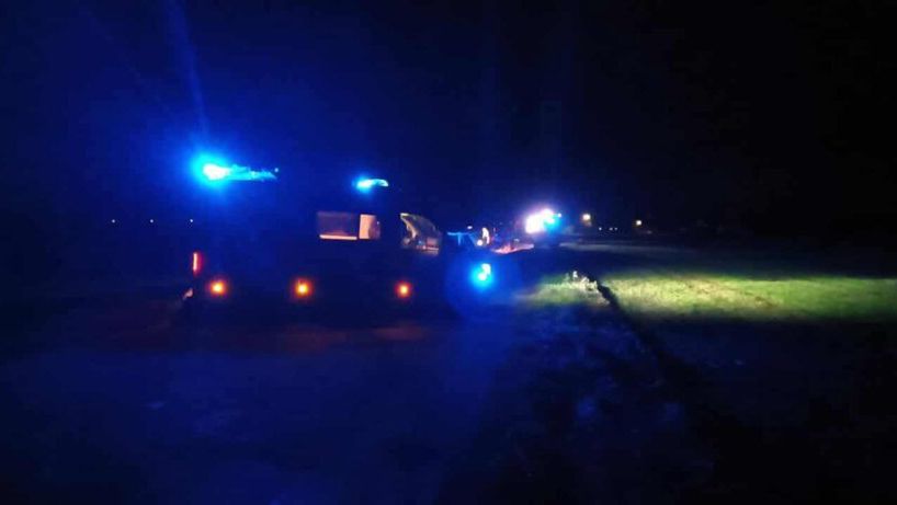 Radiowóz policyjny z włączonymi niebieskimi światłami stoi na drodze w ciemnej okolicy, oświetlając otoczenie.