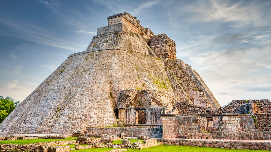 Pyramid of the Magician - Piramide del Adivino, central pyramid structure in the Maya Ruin Complex of Uxmal under blue summer sky. Pirámide del adivino is the tallest and most recognizable structure in Uxmal, Yucatan, Mexico, North America