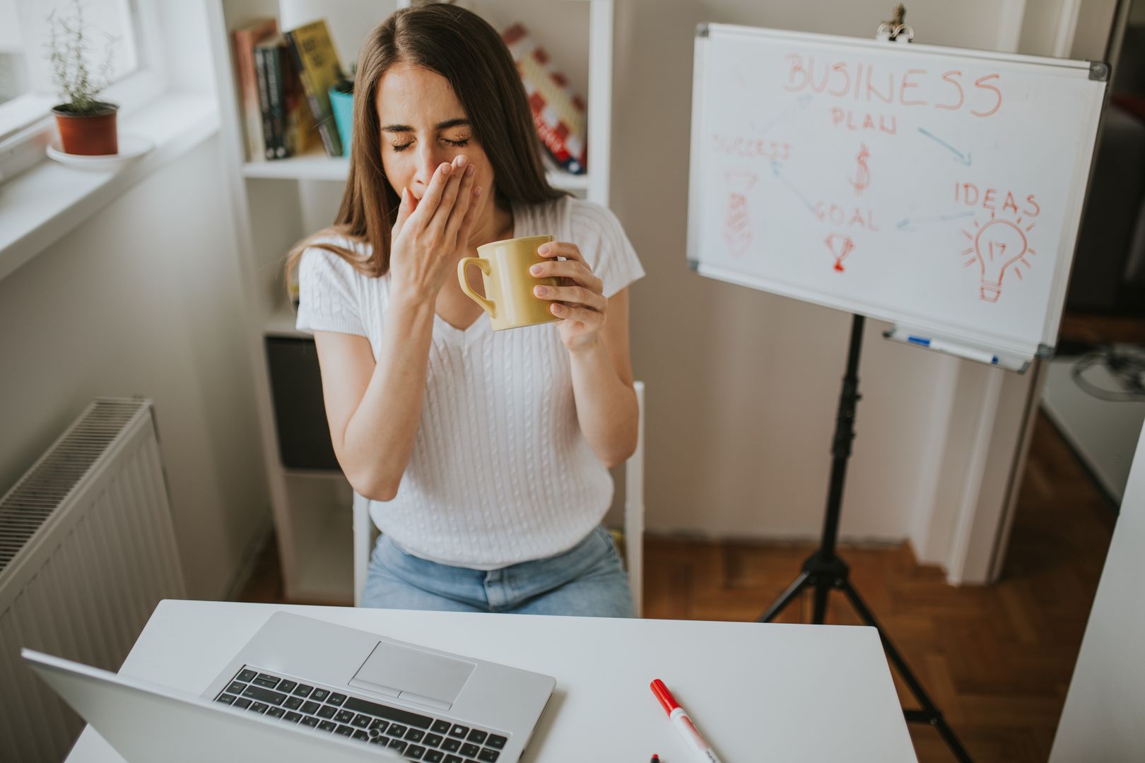 Tired woman is yawning while holding coffee.