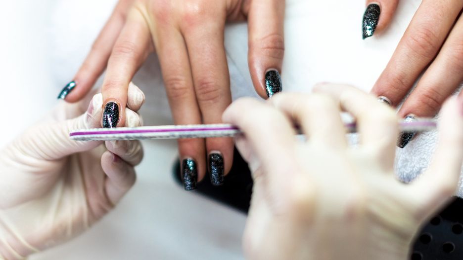 Manicurist using a file on a fingernail to remove excess cuticles and prepare it for paintingA nail file being used to tidy up a nail and remove cuticles during a manicure procedure.EXTREME-PHOTOGRAPHER