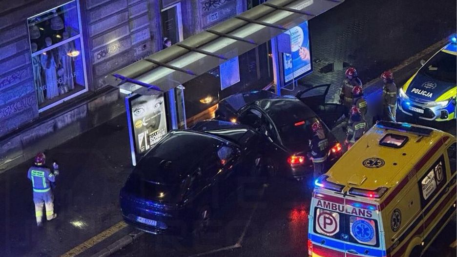 Grupa ratowników i policjantów udziela pomocy po kolizji dwóch samochodów na oświetlonej ulicy.