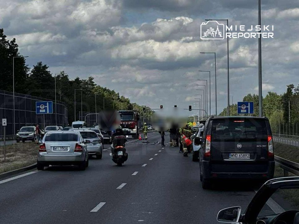 Na jezdni zatrzymane pojazdy, w tym samochód osobowy i motocykl, obok pracują służby ratunkowe.