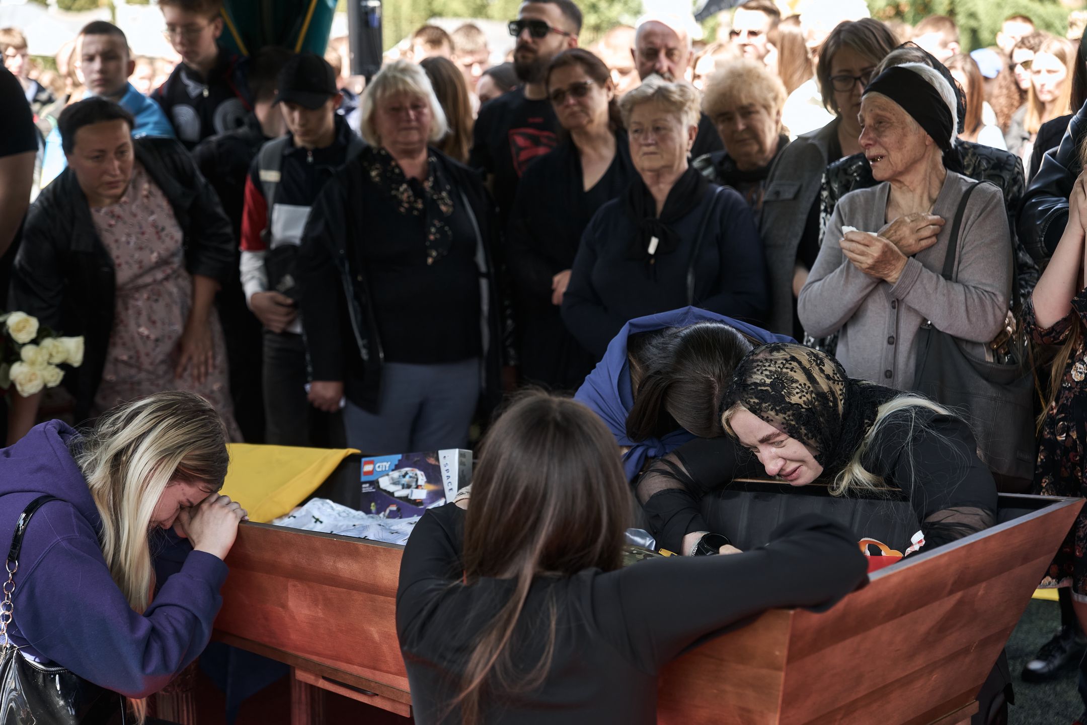 VINNYTSIA, UKRAINE - MAY 10: (EDITOR'S NOTE: Image depicts death.) A woman is comforted as she rests on the coffin at the funeral of soldier Nazar Hryntsevich "Grenka" from the "Azov" brigade on May 10, 2024 in Vinnytsia, Ukraine. During his lifetime, Nazar Hryntsevich "Grenka" was the youngest defender of Mariupol and Azovstal. He survived captivity and died at the age of 21. (Photo by Kostiantyn Liberov /Libkos/Getty Images)