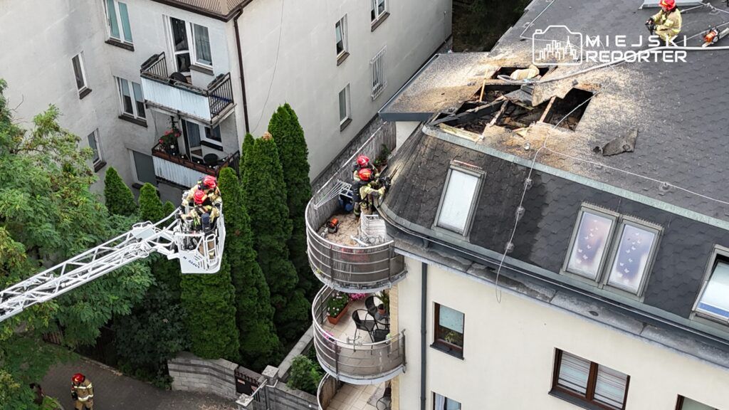 Czterech strażaków na dachu budynku, naprawiających uszkodzenia po pożarze, z drabiny strażackiej.