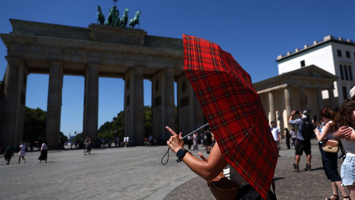 BERLIN, GERMANY - JULY 02: A woman walks holding an umbrella to protect herself from the sun in front of the Brandenburg Gate during a sweltering summer day on July 02, 2025 in Berlin, Germany. Weather forecasters are predicting record high temperatures for early July today and tomorrow as a heat wave sweeps the country. (Photo by Maryam Majd/Getty Images)