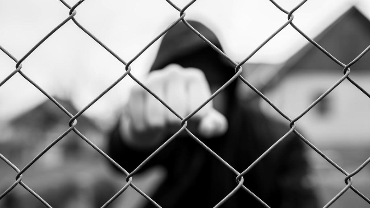 Agresywny nastolatek pokazujący pięść za ogrodzeniem