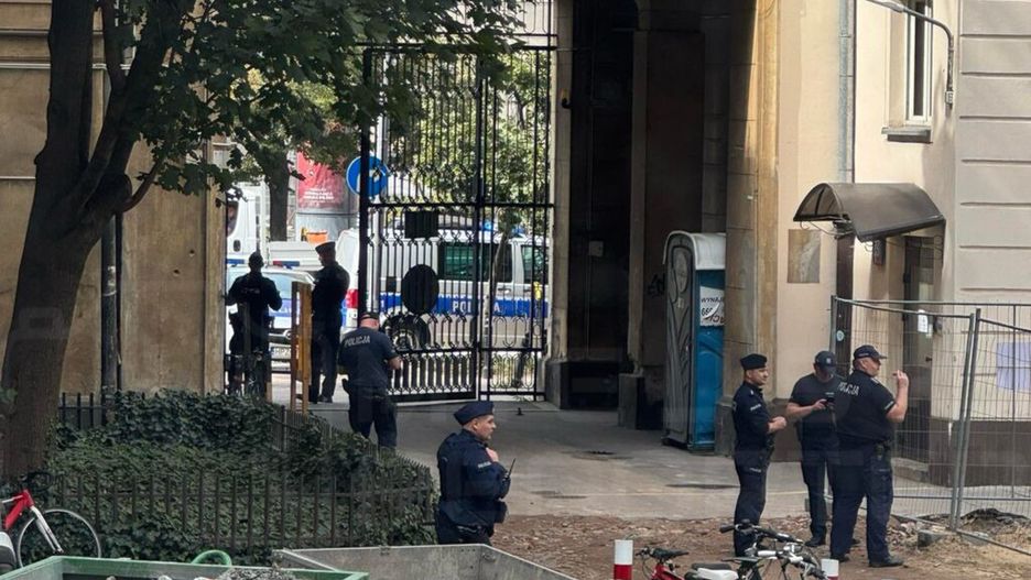 Grupa policjantów rozmawia w bramie budynku, obok stoi kontener na odpady oraz rowery.
