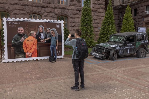 KYIV, UKRAINE - MAY 12: A man poses for photos in front of a poster made as a postage stamp depicting as a prisoner Russian President Vladimir Putin (2-L) appearing in front of judges of the International Court of Justice in The Hague, and Valerii Zaluzhnyi (L), Commander-in-Chief of the Armed Forces of Ukraine, on May 12, 2023 in downtown Kyiv, Ukraine. As the large-scale war with Russia entered its second year, the fiercest fighting was concentrated in the east and south, but residents of Kyiv and other Ukrainian cities live with the constant threat of aerial attack. (Photo by Roman Pilipey/Getty Images)Roman Pilipey