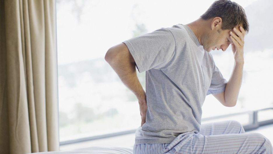Man sitting on bed with backache and headache