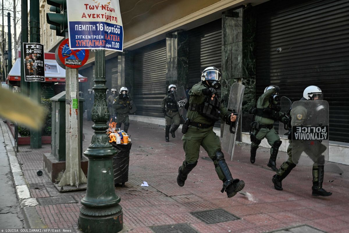 Grecki funkcjonariusz policji rzuca kanistrem z gazem łzawiącym w chwili wybuchu starć podczas 24-godzinnego strajku w Atenach 16 marca 2023 r.