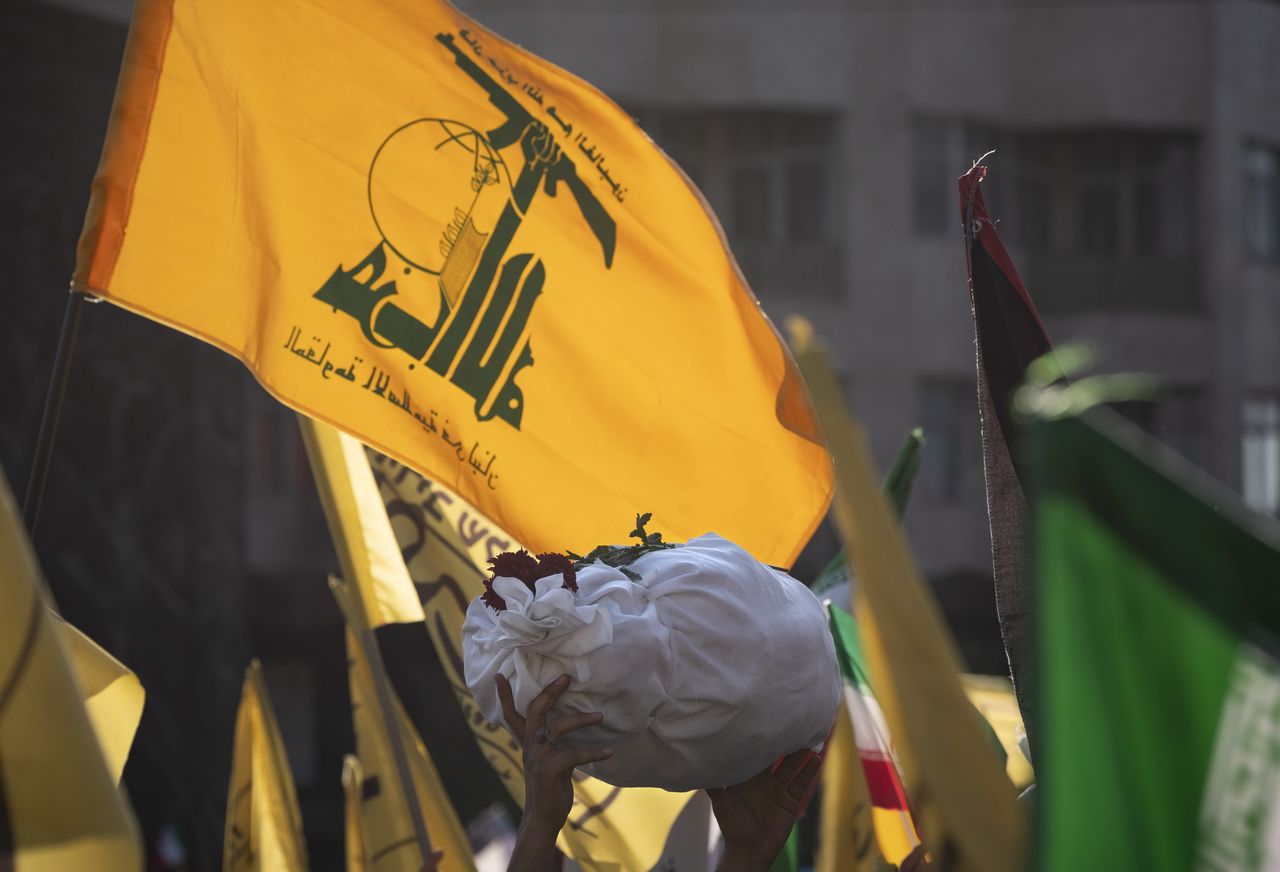 An Iranian protester holds up a shroud-wrapped package, symbolizing a body of a Palestinian child, in front of a Lebanon's Hezbollah flag at Enghelab (Revolution) square during an anti-Israeli rally in Tehran, November 18, 2023. (Photo by Morteza Nikoubazl/NurPhoto via Getty Images)