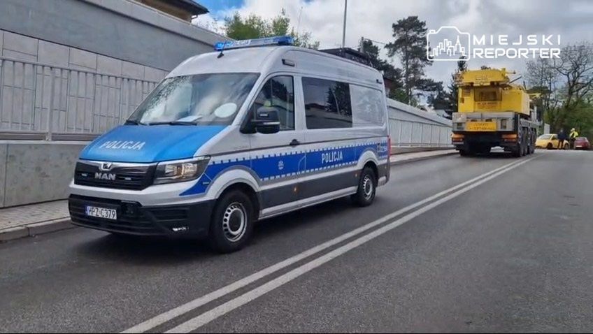 Policyjny radiowóz z niebieskimi oznaczeniami zatrzymany na drodze obok żółtej ciężarówki.