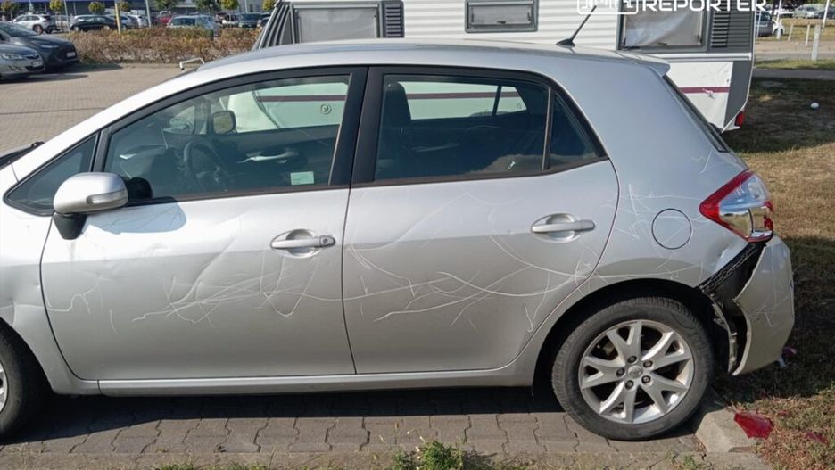 Uszkodzony srebrny samochód osobowy zaparkowany na parkingu, z widocznymi rysami na drzwiach i tylnym zderzaku.