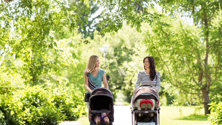 Matki spacerują z dziećmi w wózkach po parku. 