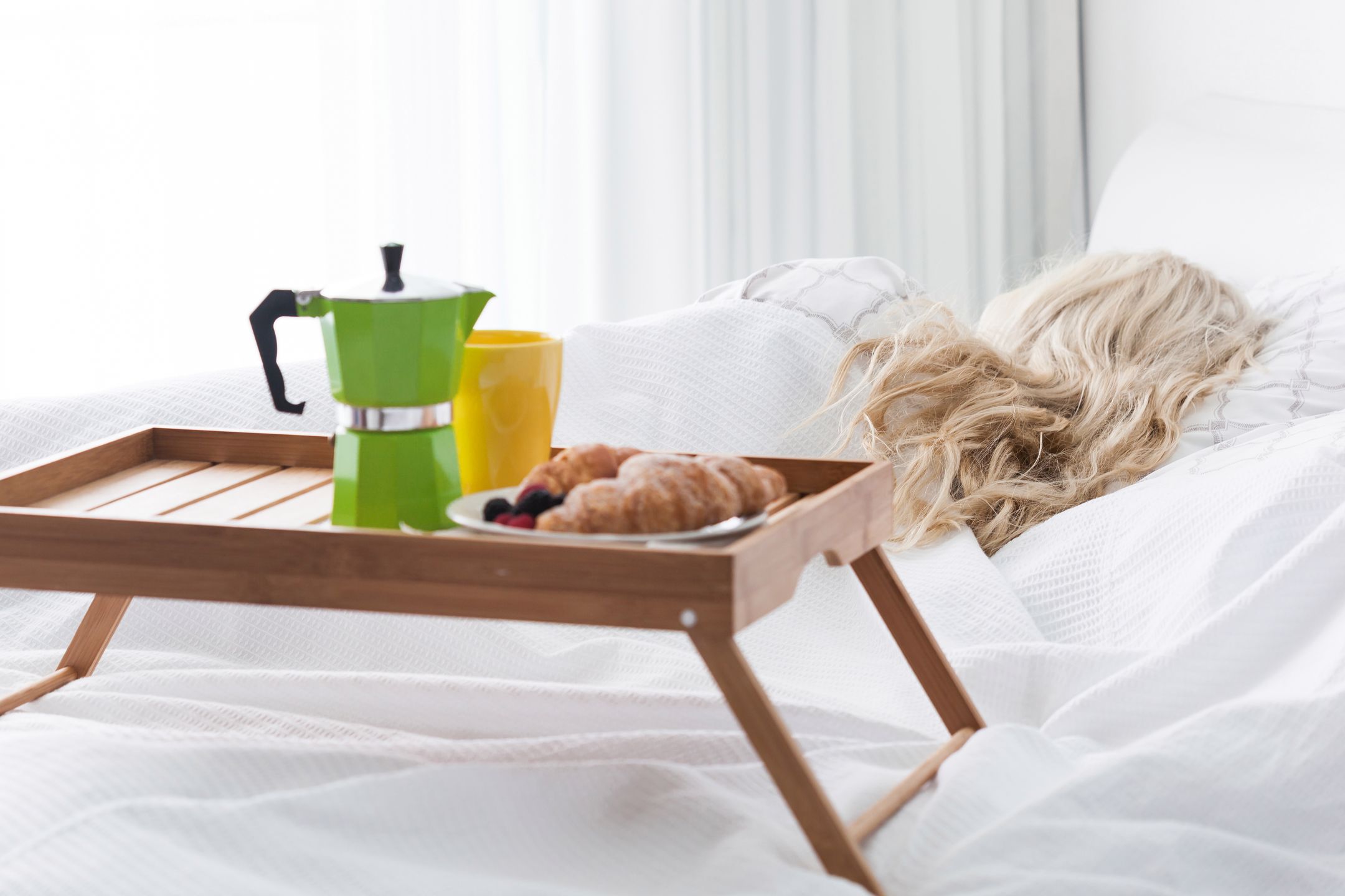 Breakfast wooden tray with coffee percolator and croissant on bed 