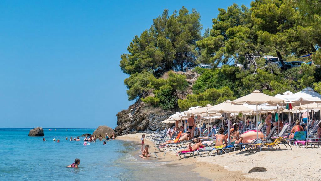Sandy Beach and beach bar with sunbeds and umbrellas called Tortuga at Sithonia peninsula, Halkidiki, Greece on 17th July 2019. The beach with the crystal clear clean seawater under the summer sun with tourists and visitors from around the world swimming, sunbathing - tanning and relaxing in the turquoise Mediterranean water of Aegean Sea, as Chalkidiki attracts worldwide tourism because of the hotel infrastructure and nature. The beach is in a beautiful natural point below the shadow of Pine trees forest and Kelifos island is visible. The location is between Lagomandra and Tripotamos near Nikiti and Neos Marmaras. (Photo by Nicolas Economou/NurPhoto)