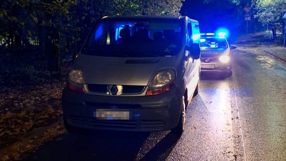 Renault stojący na poboczu drogi nocą, obok radiowóz z włączonymi niebieskimi światłami.