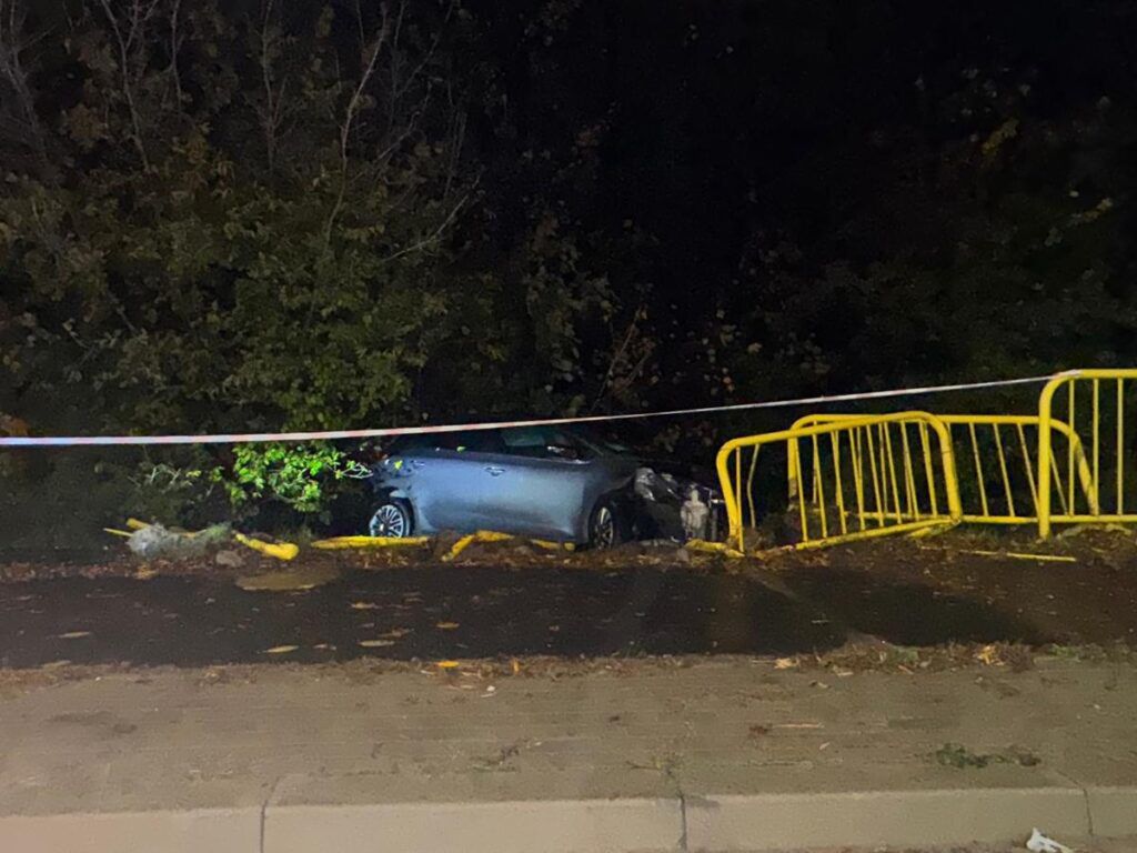 Samochód osobowy stoi na poboczu drogi, częściowo ukryty w zaroślach, otoczony żółtymi barierkami i taśmą policyjną.