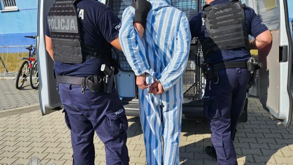 Mężczyzna w pasiastym stroju jest zatrzymywany przez dwóch policjantów przy radiowozie na parkingu.