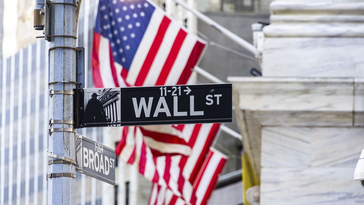 Wall Street sign inscription as seen with the American flag in the background on the road and buildings of Wall St, downtown in lower Manhattan as the area is a significant financial district for the American and the global economy, banking system and markets with the headquarters of companies and financial institutions located there like the New York Stock Exchange NYSE. New York City, USA on November 12, 2024 (Photo by Nicolas Economou/NurPhoto via Getty Images)